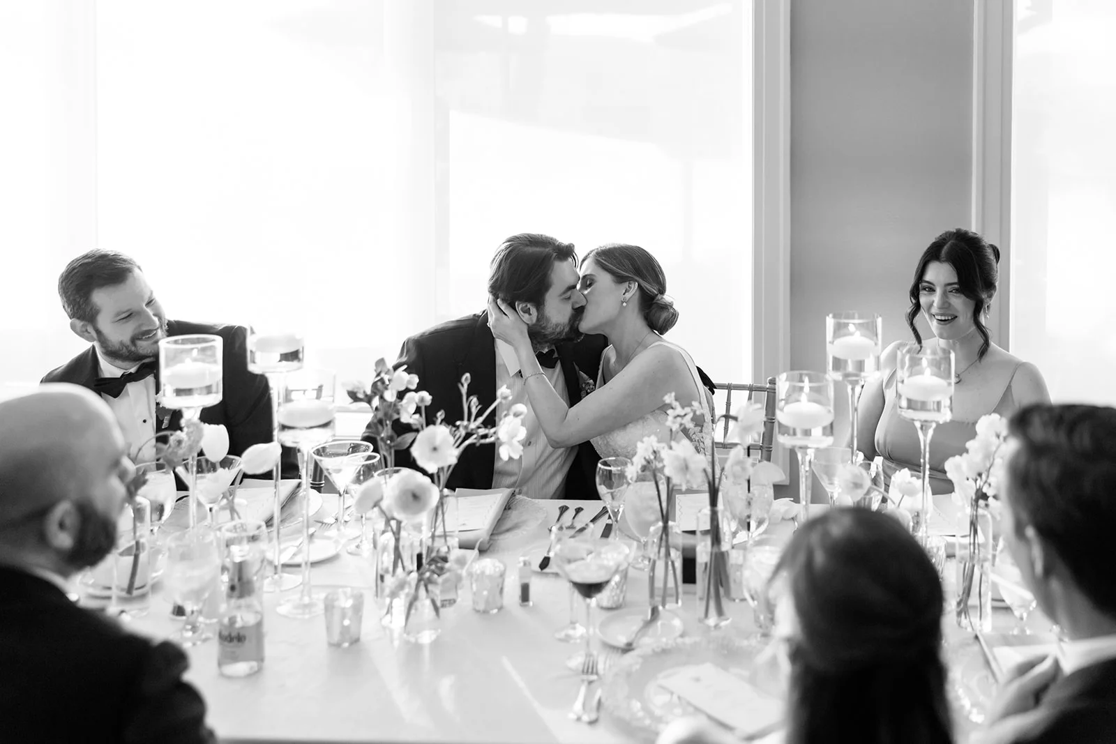 Photo of a newly married couple at wedding table kissing. Photo by C.Mae Photography.